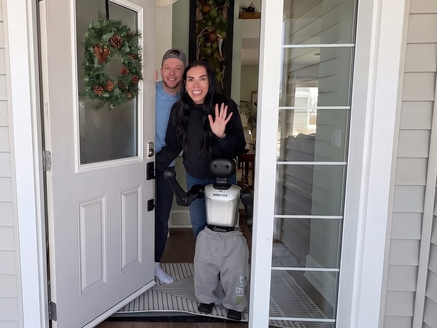Le robot devant une porte d'entrée ouverte, avec deux personnes souriantes qui saluent de la main